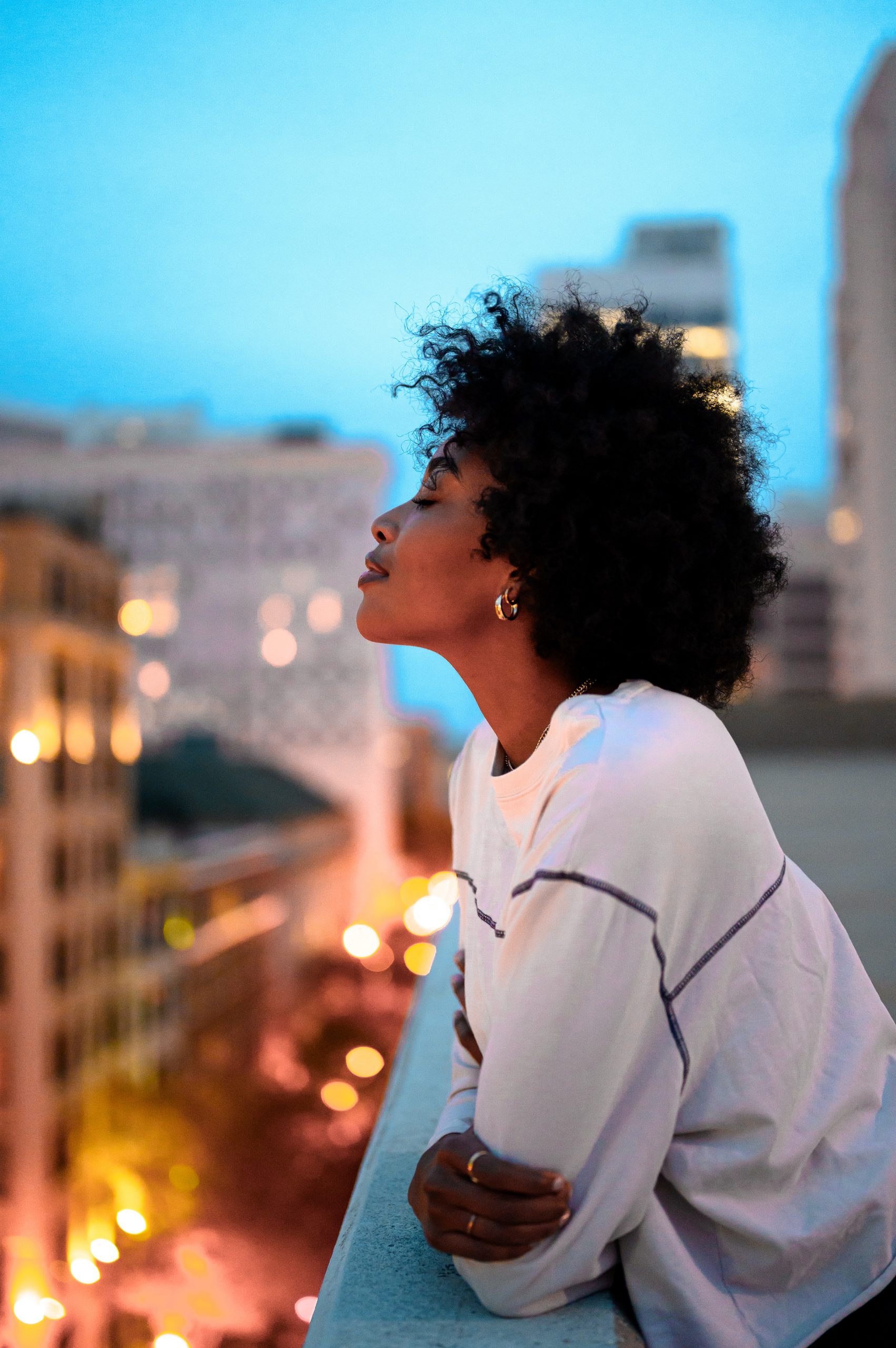 Black woman enjoying the breeze on the balcony of a building, she looks relaxed