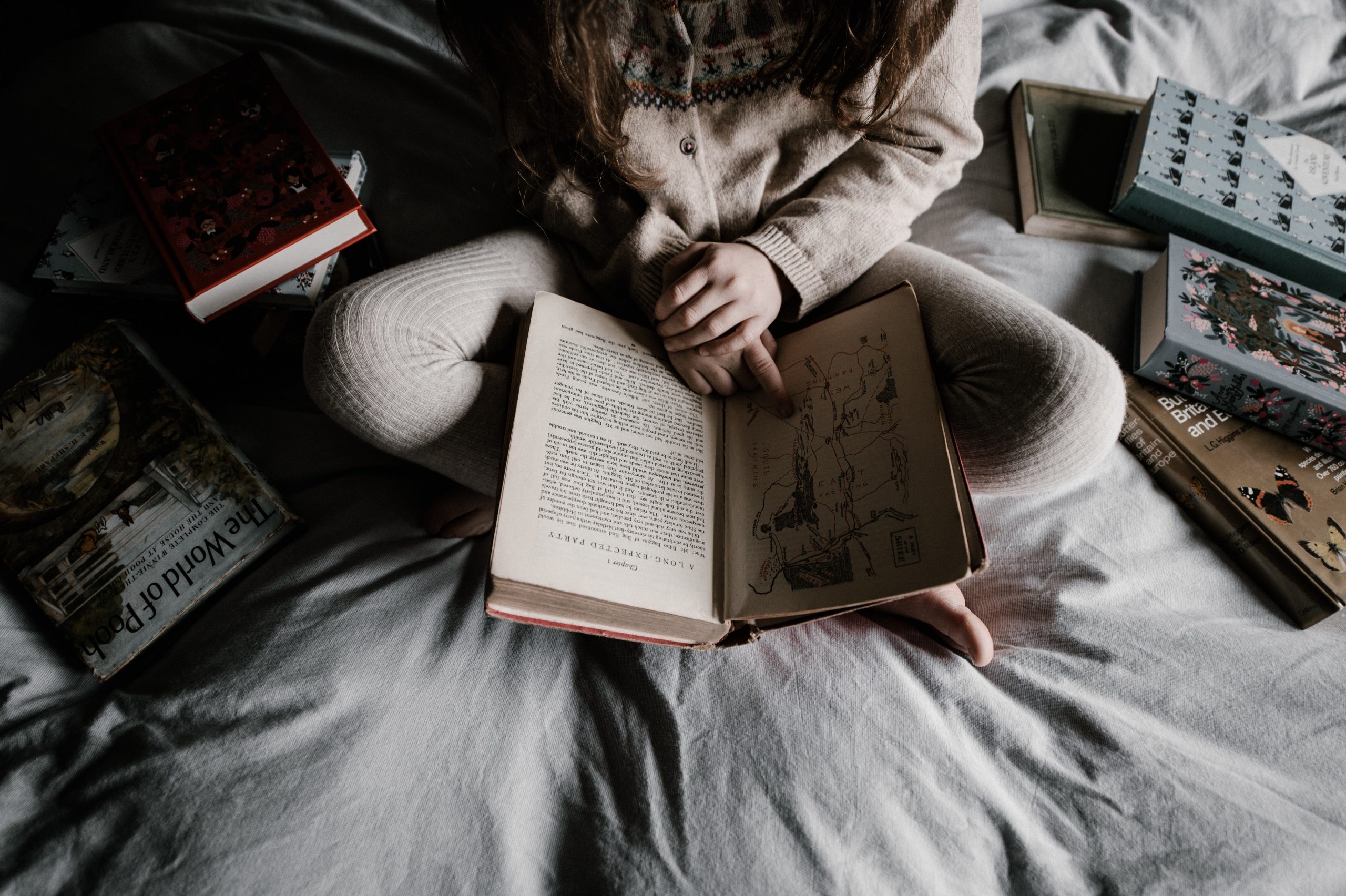 Girl in bed reading a bunch of books