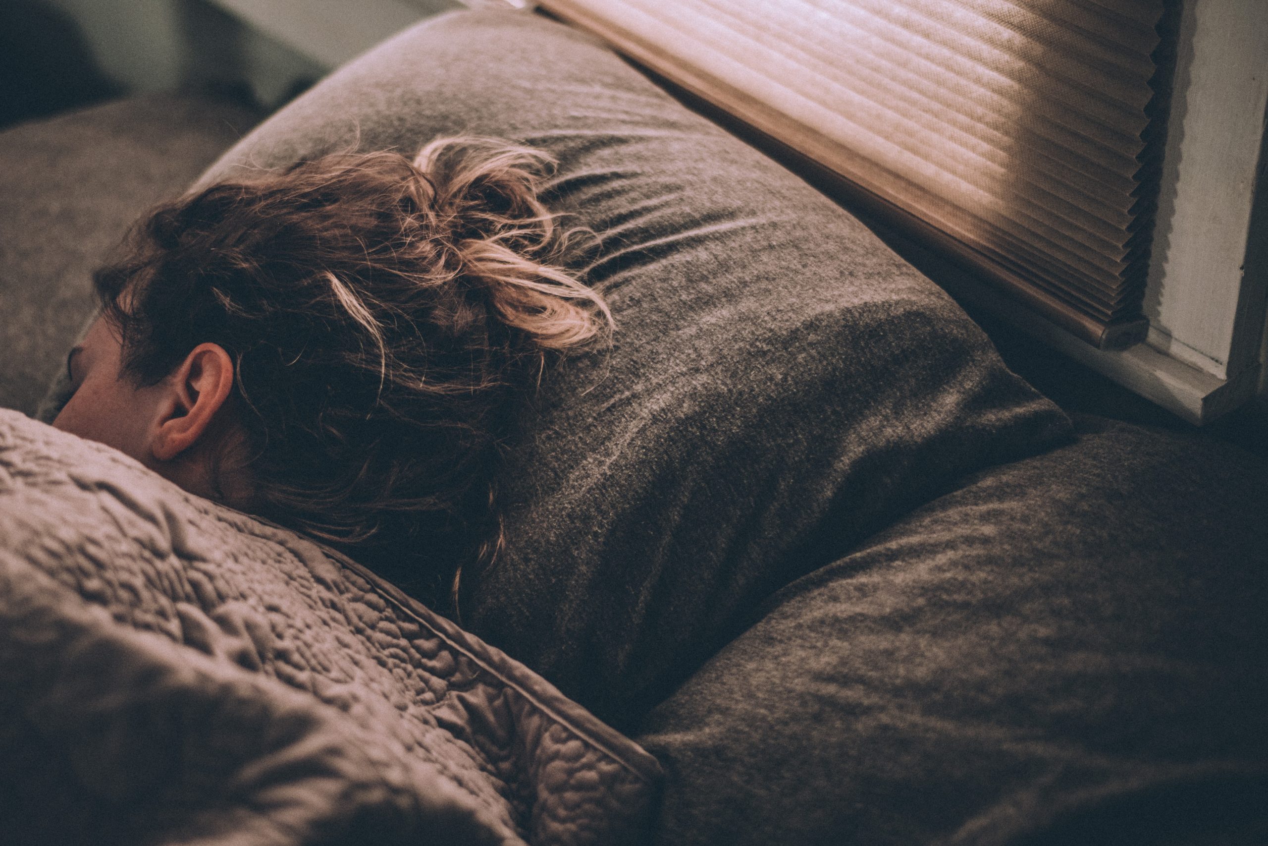 Girl sleeping in her brown sheets on a bed by the window