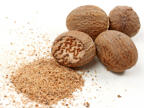 Powdered and whole nutmeg next to each other on a white surface