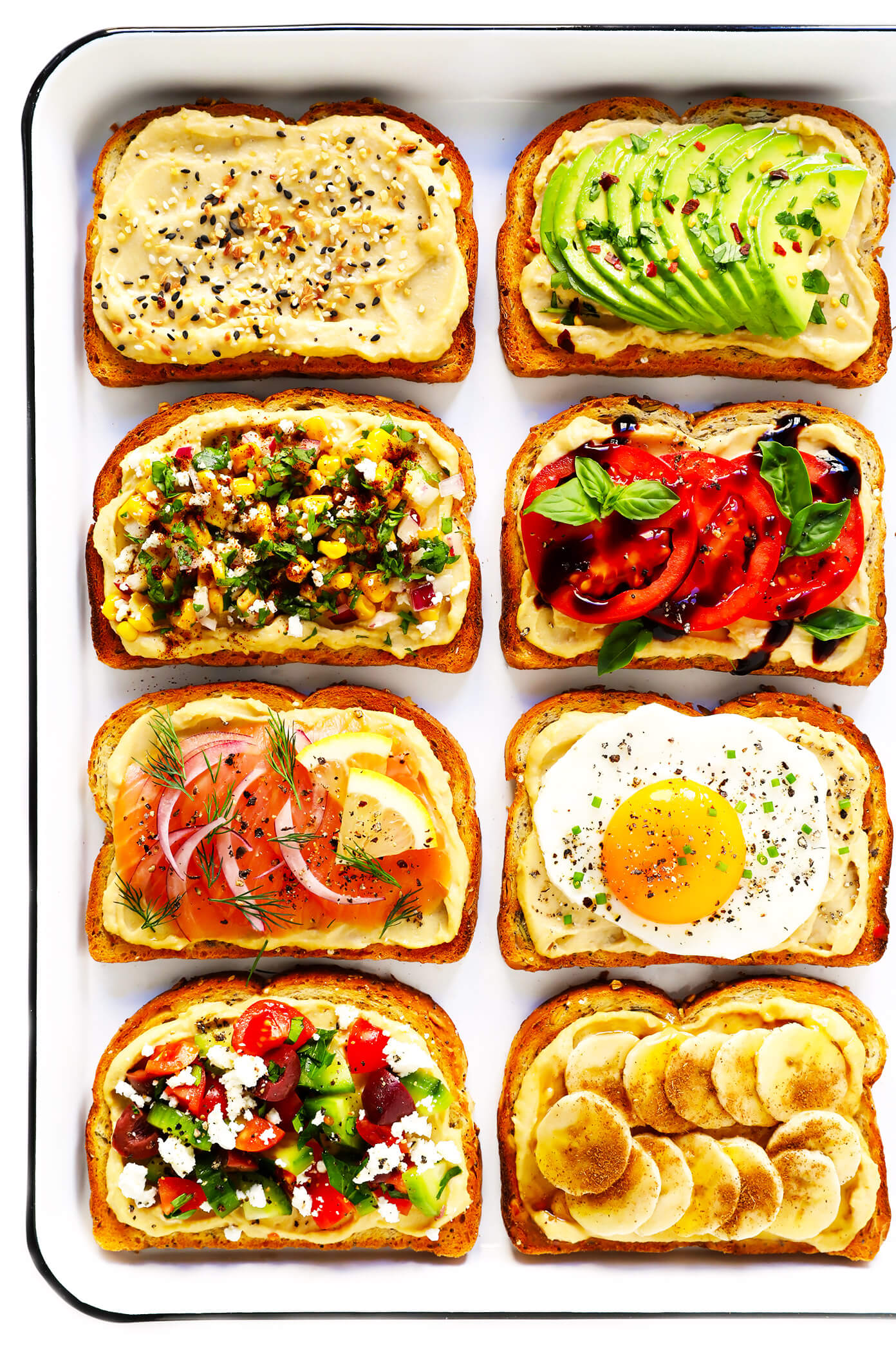 All types of hummus on toast variations on a white table