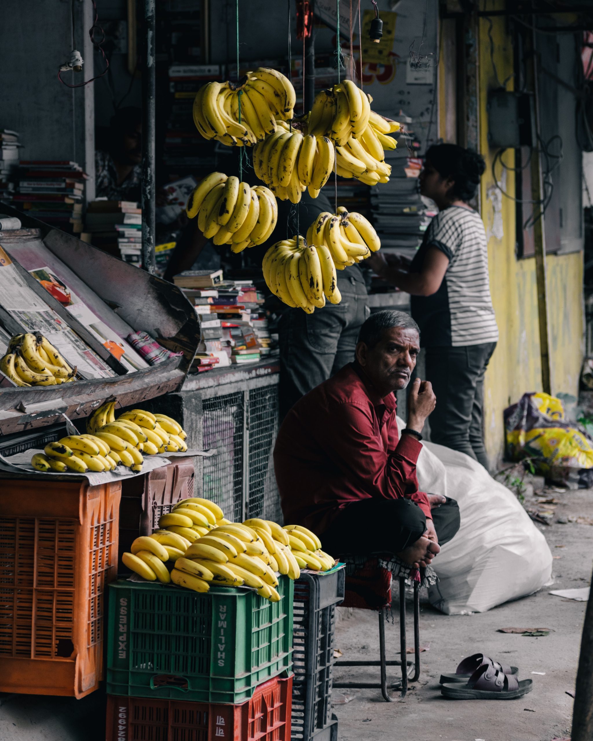 Pakistani man sitting in front of his shop selling tons of yellow bananas 
