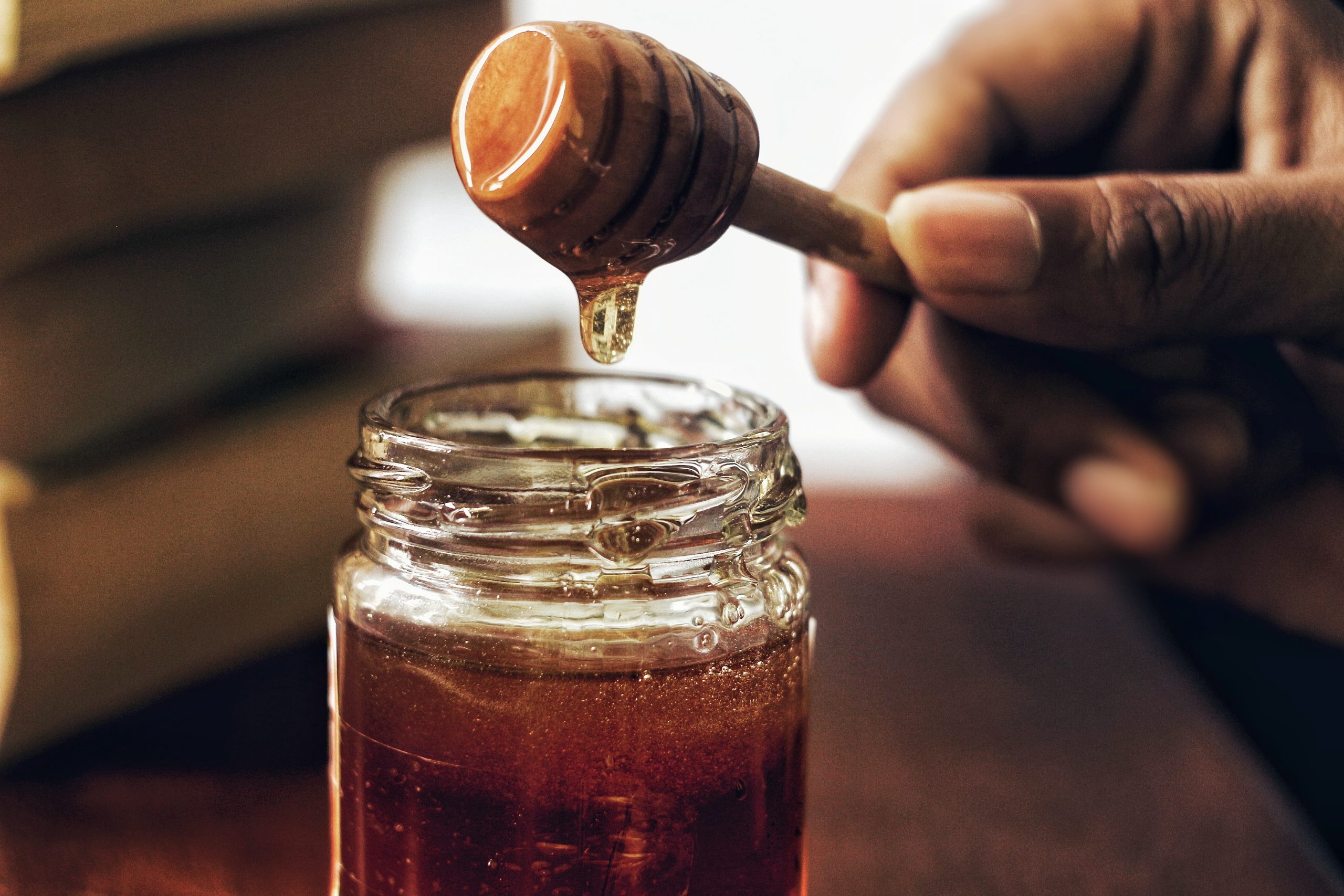 Honey in a jar with a hand scooping some out on a honey comb 