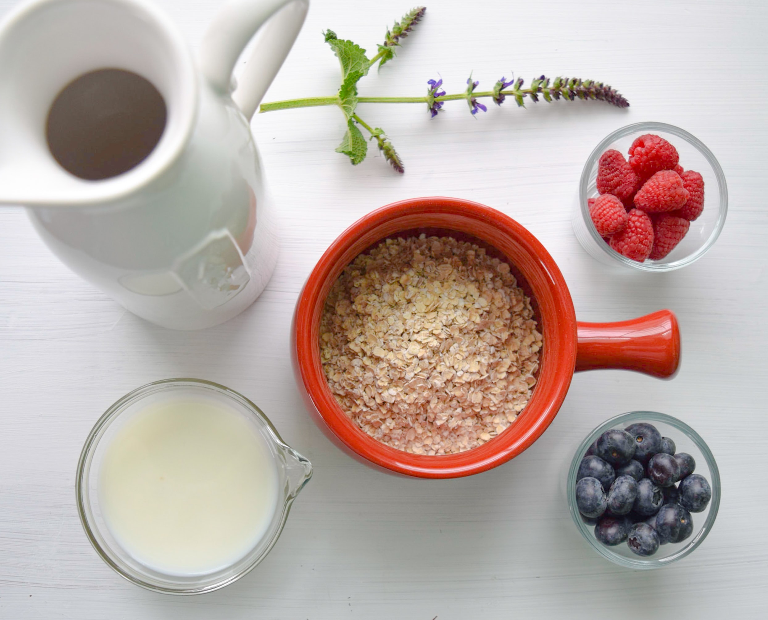 Red bowl filled with oatmeal, surrounded by fruits and a cup of milk