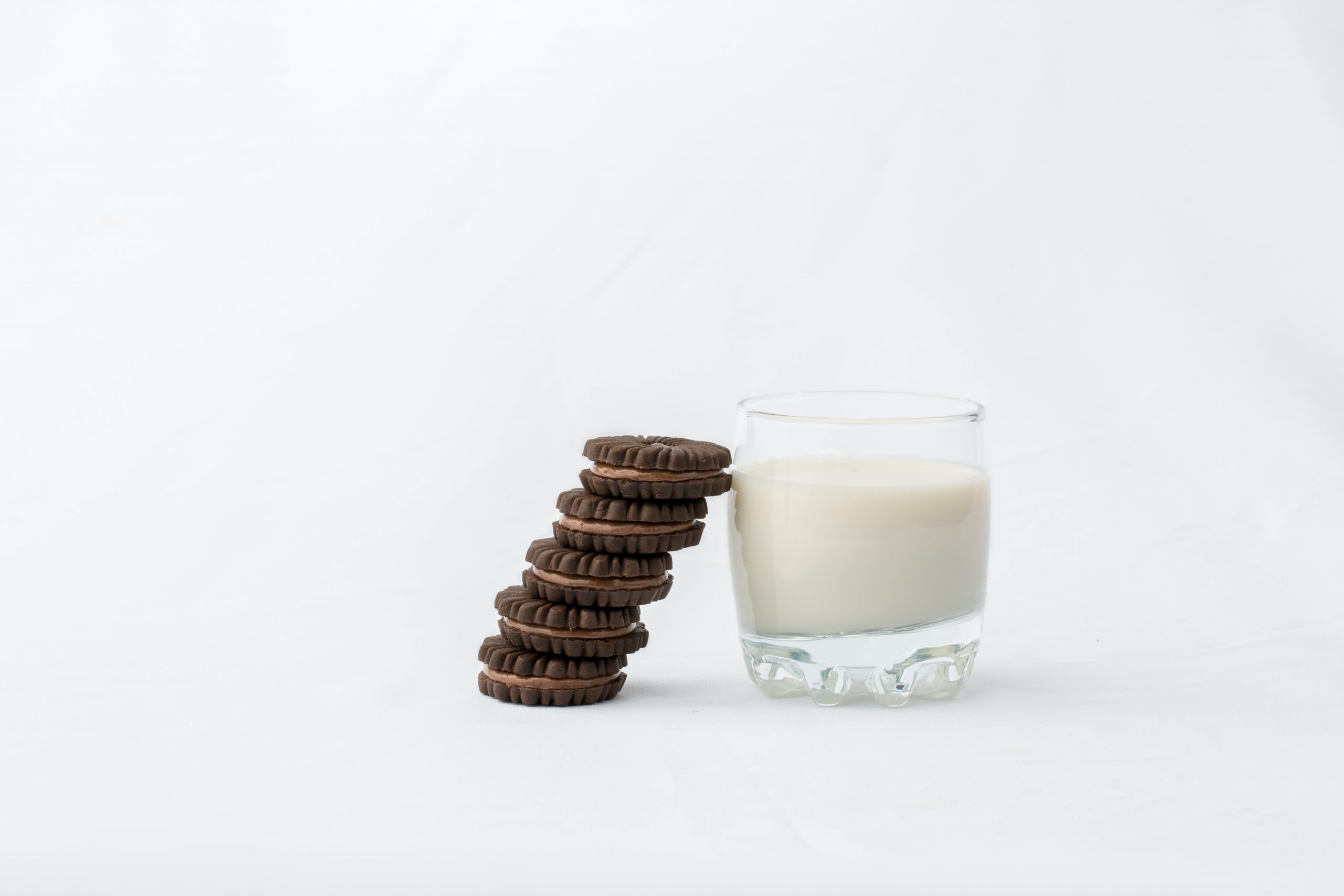 Clear glass cup filled with milk, there are 5 chocolate cookies leaned against it and the entire background is plain white
