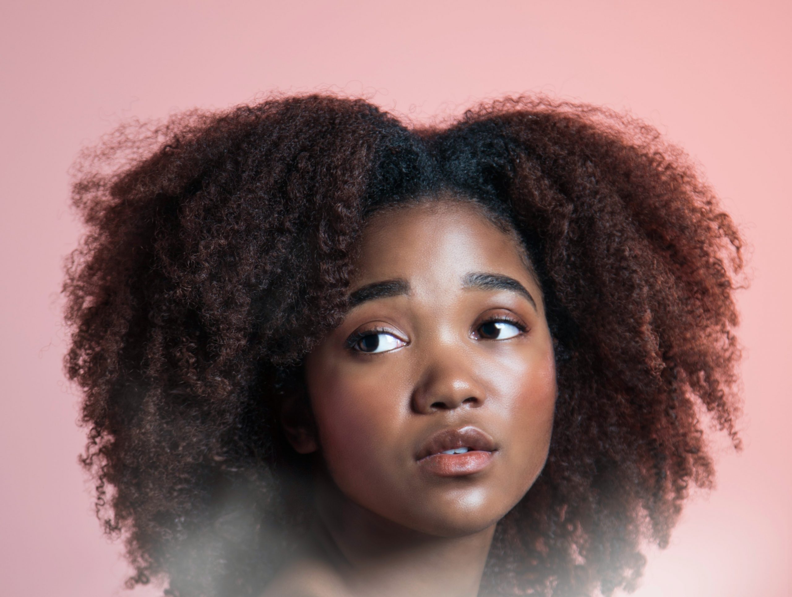 Black Woman with natural hair and clear skin looking to the left in front of a pink background
