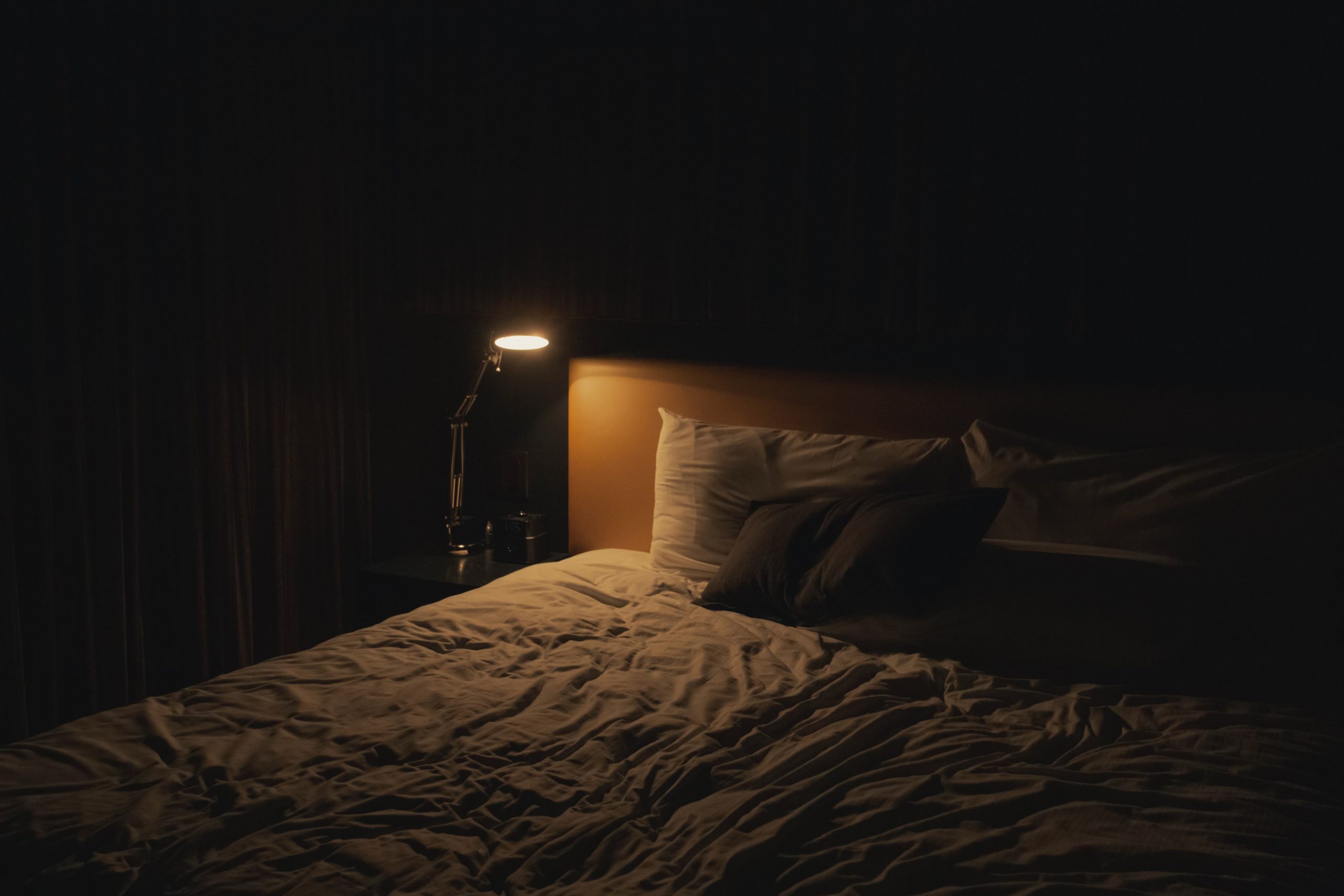 Bed in a dark room with a lamp on