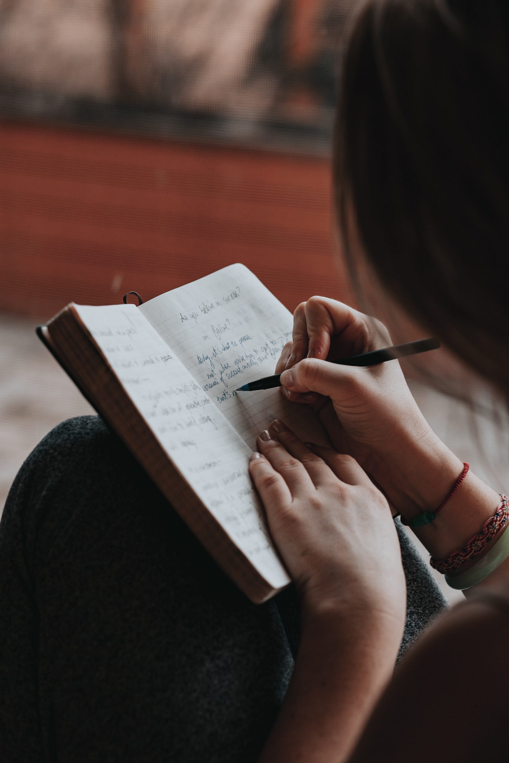 Woman writing in a diary in cursive with a pen and she has bracelets on
