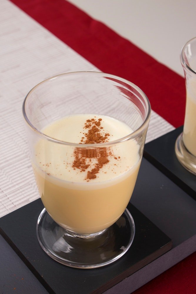 Nutmeg sprinkled on top of egg nog in a clear glass on a table