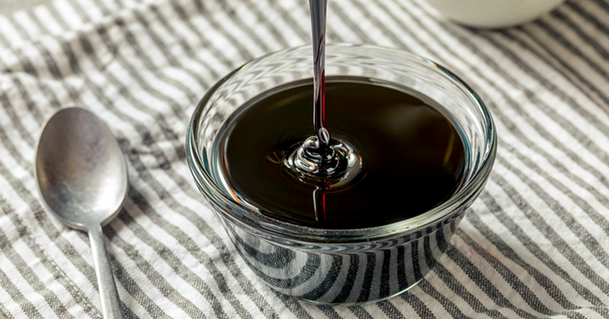 Blackstrap molasses in a glass jar on a striped surface with a silver spoon nearby